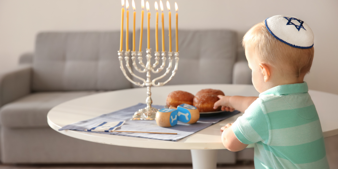 Little boy reaching for jelly rolls with hanukkiah on a table