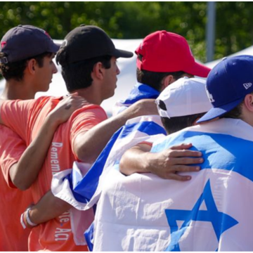 Four young teen men with arms around each other and the Israeli flag wrapped around their shoulders