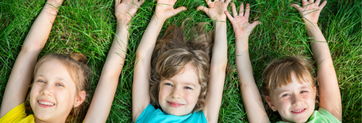 three young girls reaching for the air as they lay on the grass