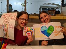 Two girls with posters they created doing acts of kindness